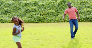 Afro-Amerikan, baba-kız güneşli parkta yakalamaca oynuyorlar, açık havada eğleniyorlar, fotokopi çekiyorlar. Aile, bağ, eğlence, oyun, doğa, mutluluk.