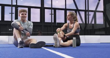 Genç bir adam ve kadın kapalı sahada dinleniyor, tenis topu tutuyor, sohbetten zevk alıyorlar. Spor, eğlence, eğlence, takım çalışması, arkadaşlık, raket.