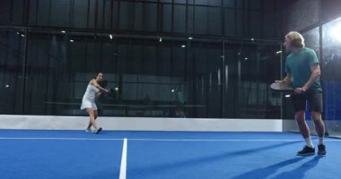 Oyuncular kapalı alandaki mavi sahada yoğun bir Padel tenis maçı yaptılar ve oyuna odaklandılar. Spor, rekabet, atletizm, raket, takım çalışması, eğlence
