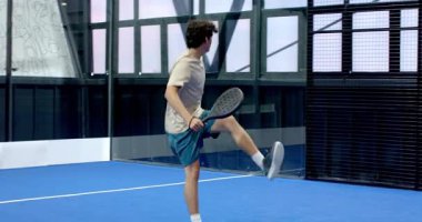 Padel tenisi oynayan genç bir adam, kapalı sahada topa odaklanıyor. raket, spor, konsantrasyon, atlet, oyun, egzersiz