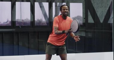 Kapalı alanda tenis oynayan, raketi tutan ve enerjik bir şekilde gülümseyen bir adam. Spor, eğlence, oyun, raket, atletik, yarışma