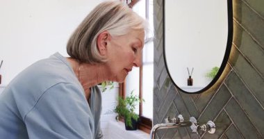 Banyoya nemlendirici sürmek, evde kendine bakım rutinine odaklanan yaşlı bir kadın. Cilt bakımı, sağlık, bakım, nemlendirici, yaşam tarzı, sağlık.