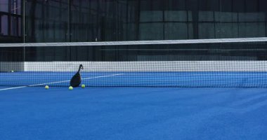Padel tenis raketi ve toplar kalenin yanındaki mavi kortta, oyun için hazır, kopyalama alanı. Spor, ekipman, eğlence, eğlence, açık hava, rekabetçi