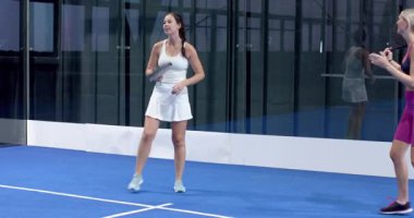 Kadınlar kapalı alanda mavi kortta Padel tenis oynuyorlar, maça odaklanıyorlar. Spor, eğlence, raket, raket, etkinlik, rekabet