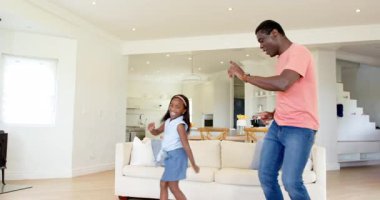 Afro-Amerikan, baba-kız oturma odasında neşeyle dans ediyor, neşeli kaynaşma zamanlarının tadını çıkarıyor. Aile, dans, mutluluk, ebeveynlik