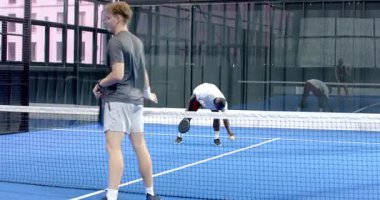 Kapalı alanda mavide Padel tenisi oynayan genç erkekler yoğun bir maça odaklanıyor. Spor, rekabet, atletizm, takım çalışması, raket, aktif