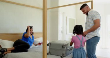 Aile bavullarını yatağın üzerine topluyor, tebessüm ve heyecanla tatile hazırlanıyor. Seyahat, tatil, valiz, hazırlık, mutluluk