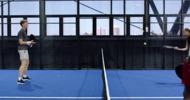 İki farklı adam kapalı alanda mavi kortta Padel tenis oynuyor ve yoğun bir maça odaklanıyor. Spor, rekabet, raket, takım çalışması, atletik, çeşitli arkadaşlar