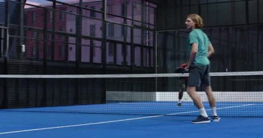 Kapalı sahada Padel tenis stratejisini tartışan genç sporcular raketleri güvenle tutuyorlar. Spor, takım çalışması, iletişim, güven, aktif, fitness