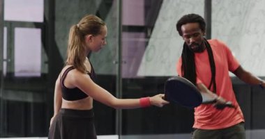 Gülen adam ve kadın kapalı sahada Padel tenis oynuyorlar, dostça bir maçın tadını çıkarıyorlar. Spor, takım çalışması, raket, aktif yaşam tarzı, rekabet, fitness