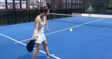 Çeşitli gruplar kapalı alanda mavi kortta Padel tenis oynuyor, takım çalışması ve stratejisine odaklanıyor. Spor, koordinasyon, eğlence, egzersiz, rekabetçi, atletik