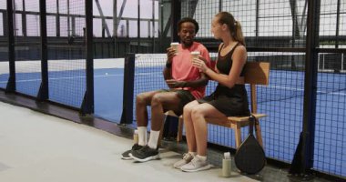 Padel tenis maçından sonra kahve molası veren çeşitli sporcular, kapalı sahada yedek kulübesinde oturuyorlar. Arkadaşlık, rahatlama, rahatlama, açık hava, spor, eğlence
