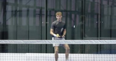 Padel tenisi oynayan genç bir adam, odaklanmış ve kapalı sahada hazır. Spor, raket, rekabet, eğitim, egzersiz, atletizm