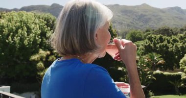 Üst düzey kadın balkonda çaydan zevk alıyor, manzaralı dağ manzarasına hayran. Rahatlama, sükunet, rahatlık, açık hava, doğa, emeklilik