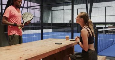 Padel tenis maçına hazırlanan çeşitli sporcular kapalı sahadaki akıllı telefonları kontrol ediyorlar. Spor, takım çalışması, rekabet, teknoloji, iletişim, hazırlık