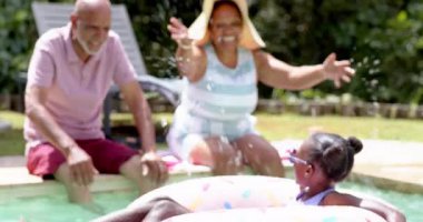 Değişik büyükbabalar torunlarıyla havuz başında eğleniyorlar, hepsi gülümsüyor. Aile, havuz başı, yaz, eğlence, kaynaşma, mutluluk