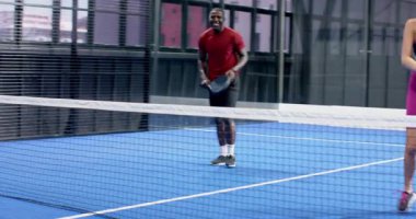 Kapalı alandaki mavi sahada Padel tenis oynayan Afro-Amerikalı adam maça odaklanmış. Spor, fitness, raket, aksiyon, rekabet, oyuncu
