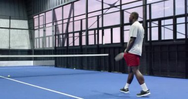 Kapalı alanda tenis oynayan bir adam raketle topa vurmaya hazırlanıyor. Spor, atletizm, fitness, oyun, eğlence, rekabet