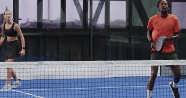 Gülen çeşitli oyuncular kapalı sahada Padel tenis maçının keyfini çıkarıyorlar, takım çalışması gösteriyorlar. Spor, atletizm, rekabet, raket, eğlence, spor