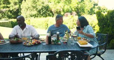 Bahçe yemeğinde eğlenen kıdemli farklı arkadaşlar, Bahçe masasında hikayeler ve kahkahalar paylaşıyorlar. Arkadaşlık, kaynaşma, piknik, bahçede, toplanma, sohbet