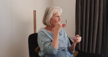 Kıdemli kadın evde huzur içinde çayın tadını çıkarıyor, sessiz yalnızlığı kucaklıyor. Yaşlılar, rahatlama, konfor, sükunet