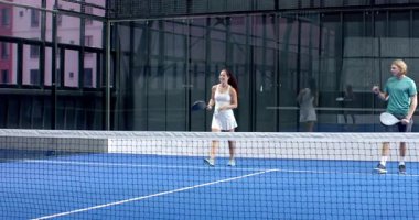 Genç yetişkinler kapalı alanda mavi kortta Padel tenis oynuyorlar, yoğun bir maça odaklanıyorlar. Spor, rekabet, takım çalışması, sporcular, egzersiz, eğlence