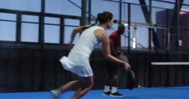 Çeşitli oyuncular kapalı sahada yoğun bir Padel tenis maçının keyfini çıkarıyorlar, odaklanmış ve kararlı. Spor, rekabet, atletizm, raket, takım çalışması, enerji