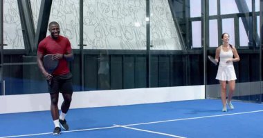 Afro-Amerikalı erkek ve kadın kapalı alanda mavi kortta Padel tenis oynuyor, odaklanmış ve hazır. Spor, takım çalışması, fitness, aktivite, Hispanik, maç