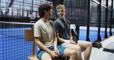 Genç adamlar bankta oturuyor, ellerinde raketle sarayda sohbet etmekten zevk alıyorlar. Spor, arkadaşlık, eğlence, eğlence, tenis, kaynaşma