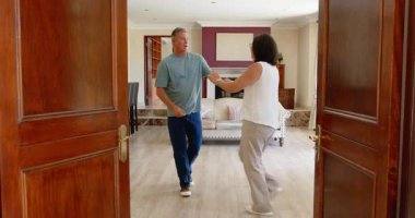 Oturma odasında neşeyle dans eden kıdemli çift, evde mutluluğu ve birlikteliği kucaklıyor. Yaşlılar, aşk, yaşam tarzı, ev, emeklilik, keyif