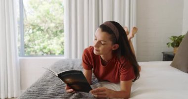 Kadın yatakta dinleniyor, kitap okuyor ve evde huzurlu bir öğleden sonra geçiriyor. Rahatlama, rahatlama, sükunet, konfor, yaşam tarzı, huzur