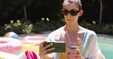 Havuzda dinlenen, güneş gözlüğü takan, akıllı telefon kullanan, güneşli günün tadını çıkaran bir kadın. Tatil, tatil, rahatlama, teknoloji, yaşam tarzı, açık hava.