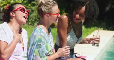 Havuz başında güneşli bir günün tadını çıkarıyor, çeşitli bayan arkadaşlar güneş gözlüğü takıyor ve gülümsüyor. Tatil, tatil, rahatlama, arkadaşlık, yaz, yaşam tarzı.