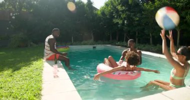 Farklı arkadaşlar plaj topu ve şişirilebilir yüzeyle havuz partisinden zevk alıyorlar, birlikte gülüyorlar. Yaz, dinlenme, rahatlama, havuz kenarı, arkadaşlık, eğlence.