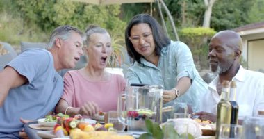 Bahçe yemeğinde eğlenen, gülümseyen ve tabletteki anılarını paylaşan farklı yaşlılardan oluşan bir grup. Yaşam biçimi