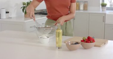 Kadın modern mutfakta cam kasedeki malzemeleri taze meyvelerle karıştırıyor. Aşçılık, aşçılık, gurme, sağlıklı, hazırlık, yaşam tarzı