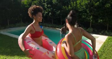 Havuz partisinde, çeşitli arkadaşlar şişirilebilir su sıçratır, güler ve eğlenirler. Yaz, açık hava, havuz kenarı, eğlence, dinlenme