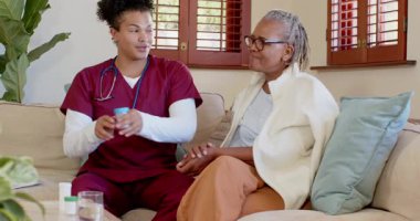 Önlüklü bakıcı evde yaşlı kadına yardım ediyor, sıcak sohbetler ediyor. Bakım, sağlık, arkadaşlık, destek, ev bakımı, yardım