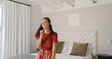 Kadın kulaklıklı müzikten hoşlanıyor, rahat yatak odasında mutlu bir şekilde dans ediyor, evde. Rahatlama, mutluluk, yaşam tarzı, rahatlık.