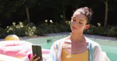 Kadın havuz başında selfie çekiyor, içki tutuyor, açık havada güneşli bir günün tadını çıkarıyor. Tatil, tatil, rahatlama, yaz, havuz başı, yaşam tarzı.