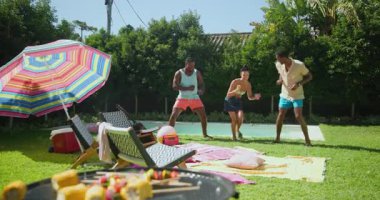 Çeşitli arkadaşlar havuz kenarında neşeyle dans ediyor, yaz gününün tadını çıkarıyor ve yakınlarda barbekü var. Kutlama, parti, açık hava, eğlence, eğlence, eğlence