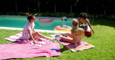 Çeşitli bayan arkadaşlar havuzda dinleniyor, plaj topu ve havlularla güneşli bir günün tadını çıkarıyorlar. Tatil, eğlence, yaz, açık hava, rahatlama.