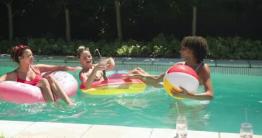Çeşitli bayan arkadaşlar havuz gününün tadını çıkarıyorlar, şişme kutularda yüzüyorlar, plaj topuyla oynuyorlar. Yaz, tatil, dinlenme, boş zaman, havuz kenarı, güneş ışığı.