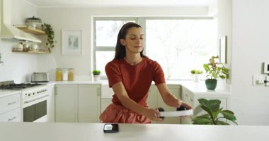 Evde, kulaklıkla müzik dinlerken mutfakta neşeyle dans eden genç bir kadın. Dans, yaşam tarzı, enerjik, mutluluk, rahatlık