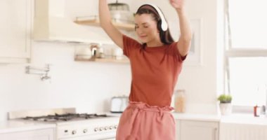 Mutfakta kulaklıkla müzik dinlerken neşeyle dans eden genç bir kadın. Mutluluk, yaşam tarzı, tasasız, keyif, ev, eğlence