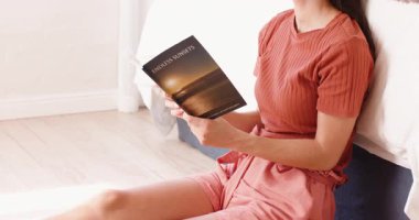 Yerde oturmuş kitap okuyan, aydınlık yatak odasında dinlenen bir kadın. Rahatlama, rahatlama, edebiyat, iç mekan, yaşam tarzı, konforlu