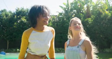 Güneşli bir günde havuz başında gülümseyen ve sohbet eden iki bayan arkadaş. Arkadaşlık, rahatlık, sohbet, yaz mevsimi, mutluluk, rahatlama.