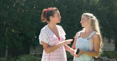 İki bayan arkadaş dışarıda yürüyor, gülümsüyor ve güneşli günün tadını çıkarıyorlar. Mutluluk, doğa, güneş ışığı, eğlence, çeşitli kadın arkadaşlar, yaşam tarzı