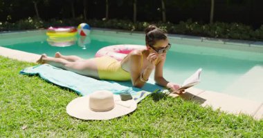 Havuzda dinlenen, güneş gözlüklü bir kadın güneşli bir günde kitap okuyor, fotokopi çekiyor. Boş zaman, yaz, tatil, dinlenme, güneşlenme, açık hava.