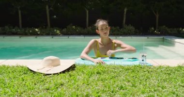 Havuzda dinlenen, yakınlarda şapkası ve içkisiyle güneşli bir günün tadını çıkaran bir kadın, fotokopi odası. Tatil, tatil, havuz başı, yaz, dinlenme, güneş banyosu.